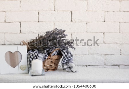 Lavender in a wicker basket,empty frame and a candle, against a white brick wall. Shabby chic interior decor for farmhouse. Provence home decoration.