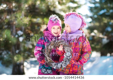 Beautiful white winter picture in a snow-covered forest in nature with children. Two sisters twins in bright jackets and hats are holding a wreath of twigs and cones. Girls are played in the winter.