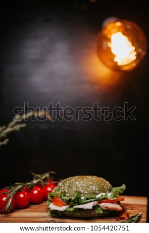 Hamburger with a green muffin slices of ham, tomatoes and lettuce leaves. wooden background.