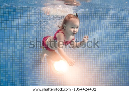 Little baby, girl swimming under water in paddling pool. Diving baby. Learning infant child to swim. Enjoy of swimming and bubbles.