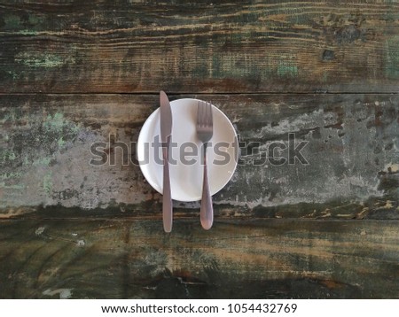 White plate with knife and fork placed in the middle of wooden table.