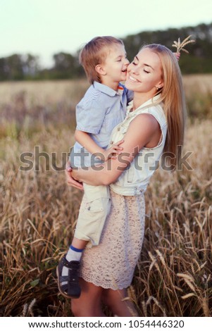 Young blonde beautiful mother walking with her smiling son on the golden field. Happy family and sunny day