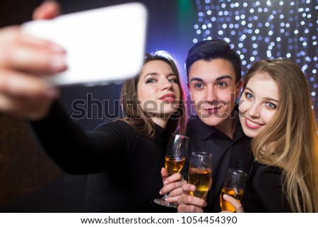 Three young men and two women  with glass champagne make selfie photo on smartphone celebrate a birthday have fun in a nightclub at a party
