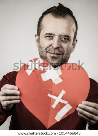 Healed love. Valentines Day concept. Adult smiling man holding big red heart with plaster. Male healing relationship.