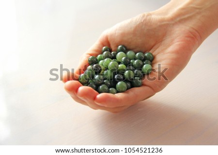 Natural green jade nephrite mineral stones beads. The green jade stone lies in the hands. Hands holding stone on white background. Green and grassy natural background made of round stone beads.