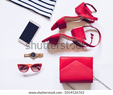 fashion blog concept on white background. flat lay of a minimal set of female accessories:golden wrist watch, red mid heel sandals with ankle strap, clutch bag, mobile phone, sunglasses, striped shirt