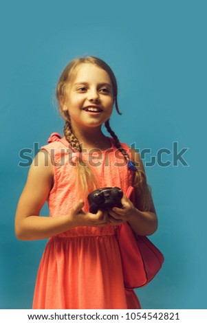 Kid with happy face. Girl with black alarm clock and pink bag. Pupil with braids, isolated on blue background. Back to school and childhood concept