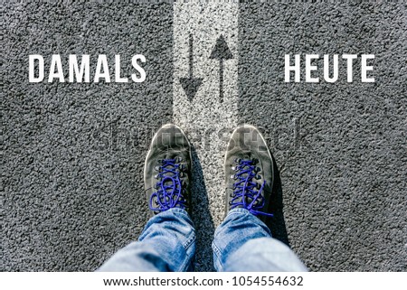 Reaching a crossroads having to choose between damals and heute in german meaning then and now symbolized by two feet standing on two different colors with arrows on pathway from above