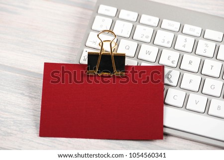 Business card in red color with golden clamp on computer keyboard. Mockup.