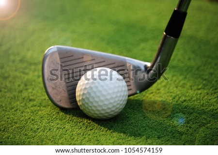 golf club and golf ball close up in grass field with sunset.