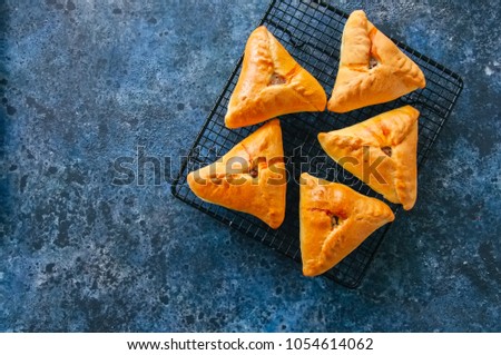 Homemade baked uchpuchmak (samsa) with meat and potato served on a wire rack on a blue sackcloth background. Top view and copy space.