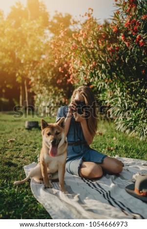 Young hipster girl taking a photo on vintage film camera while enjoying holidays in the city park with shiba inu dog, lifestyle enjoyment weekend concept, sunny weather