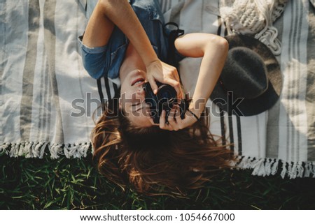 Shot of young happy smiling girl with long hair lying on grass taking a photo on vintage film camera, beautiful smiling hipster girl chilling in the park, lifestyle relax and holidays