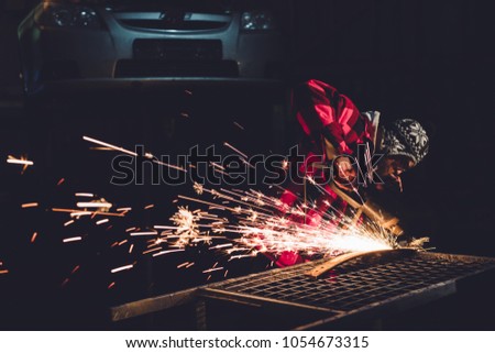 Worker Using Angle Grinder in Factory and throwing sparks. The employee of the service station produces body repair with a welding machine in hand sparks