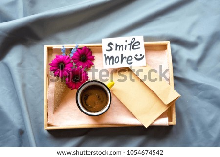 A wooden tray on the bed with flowers ,coffee and a note with smile more text on an envelope