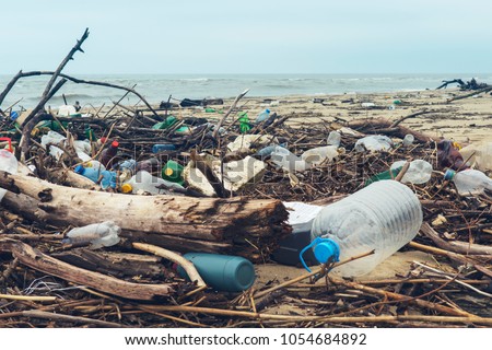 Spilled garbage on the beach of the big city. Empty used dirty plastic bottles. Dirty sea sandy shore the Black Sea. Environmental pollution. Ecological problem. Bokeh moving waves in the background Royalty-Free Stock Photo #1054684892