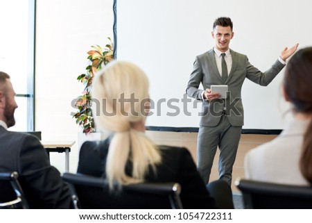 Portrait of successful young businessman giving presentation standing by white screen  in conference hall