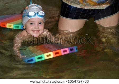 smiling little girl in swimming cap and glasses for the
pool is swimming in the pool with the help of swimming
board
