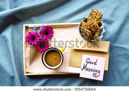 A wooden tray on the bed with flowers ,coffee ,Granola bars and Good Morning text on a note