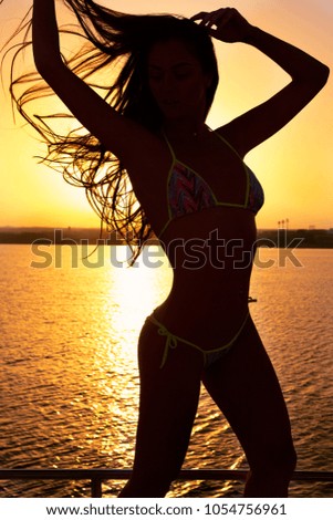 Silhouette of beautiful fit girl playing with her hair on the sea at sunset