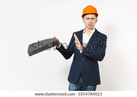 Dissatisfied annoyed tired businessman in dark suit, protective hardhat showing stop gesture with palm to black folder for papers document isolated on white background. Male worker for advertisement