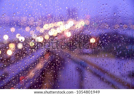 The blurred traffic jam background behind the window with raindrops at night.
