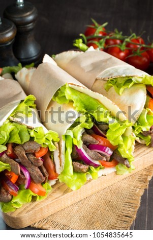 Photo of Mexican sandwich food, burrito, fajita, tacos, wrap made of tortilla, beef, chicken, fresh vegetables on rustic wooden background. Fast food concept. Healthy lunch snack. Copy space. 