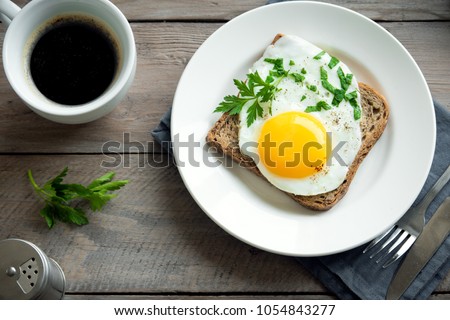 Fried Egg on Wholegrain Toast and cup of Coffee for Breakfast. Fried egg with bread on plate over wooden table, top view, copy space. Royalty-Free Stock Photo #1054843277