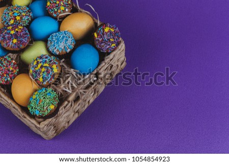 Easter eggs and Easter cupcakes in a basket on a purple background.