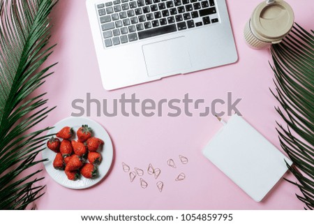 Working space: Laptop, palm leaf, coffee and strawberry on a pink background. Top view, flat lay, space for text