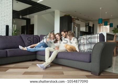 Smiling parents with kids having fun with laptop in cozy living room interior, couple with children son and daughter using computer on sofa at home, happy family relaxing together shopping online