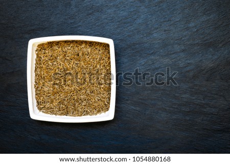 Dry caraway seeds in white plate placed on deep blue and black stone background surface with free space