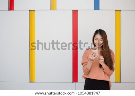 Young woman using smartphones and smiling while standing against wall.