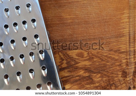 The chrome grater lies on the cutting board with a lot of scars from the ax and knife. Background image for cooking recipes