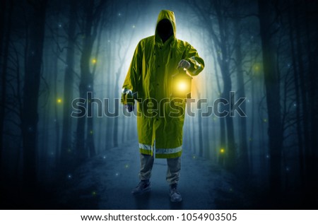 Man in raincoat coming from dark forest with glowing lantern in his hand concept