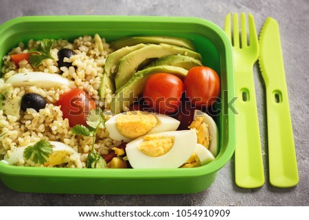 Lunch box with bulgur, avocado, eggs and tomatoes.