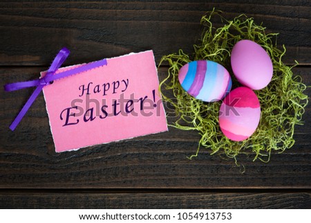 Happy Easter card with three Easter Eggs in Dyed Pink, Blue, lavender and Purple in green nest on rustic dark wood background.  Horizontal flat lay photo from looking down above view