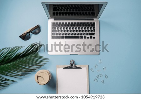 Working space: Laptop, palm leaf, coffee and strawberry on a blue background. Top view, flat lay, space for text