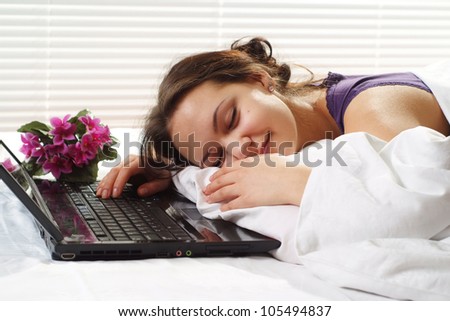 Beautiful Caucasian woman sleeping in a bed of laptop on a light background