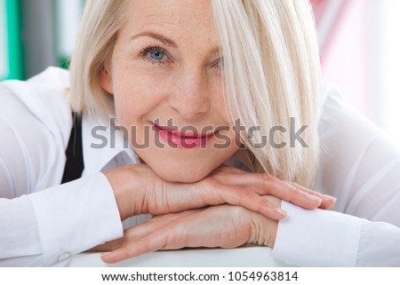 Lovely middle-aged blond woman with beaming smile sitting at office looking at the camera Royalty-Free Stock Photo #1054963814
