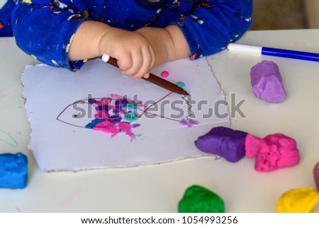
Child hands playing with colorful clay .Baby hand of Little girl drawing funny fish on white paper.