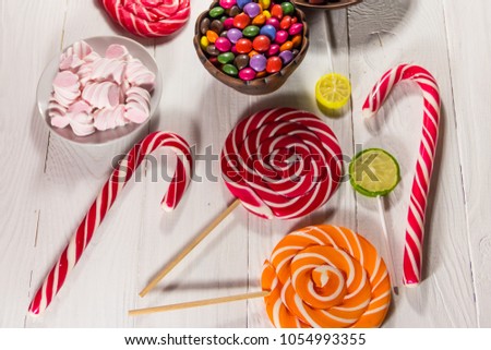 Colorful chocolate candies, lollipops, candy cane and marshmallows on white wooden table