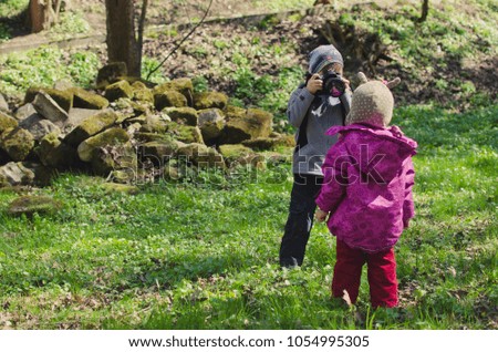A boy photographs a little girl in a park