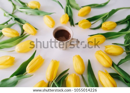 A coffee cup in a frame of yellow tulips on white background. Flat lay, top view. Concept of holiday, birthday, Easter, March 8. 