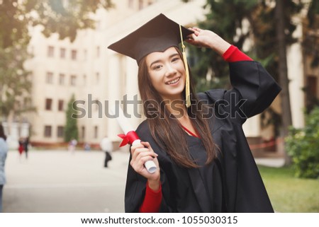 Young smiling woman on her graduation day in university holding diploma. Education, qualification and gown concept.