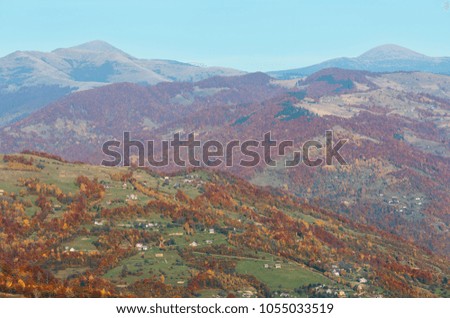 Autumn Carpathian Mountains landscape with multicolored trees on slope, village, Goverla and Petros mountains in far (view from Rakhiv pass, Transcarpathia, Ukraine).