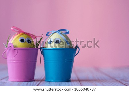 Funny painted eggs with eyes in small buckets on pink background. 