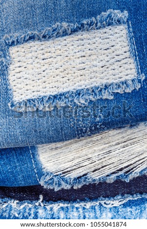 Stack of torn denim jeans with holes. Ripped Destroyed Torn Blue denim cloth background. White  stitching  on torn denim blue jeans patch.