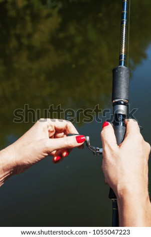 Female hand holds fishing spinning outdoors against the background of a water surface