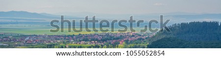Large panorama of a small town in Transylvania, Romania, Eastern Europe. Green and yellow fields, old traditional villages and forested mountains on a clear summer day.